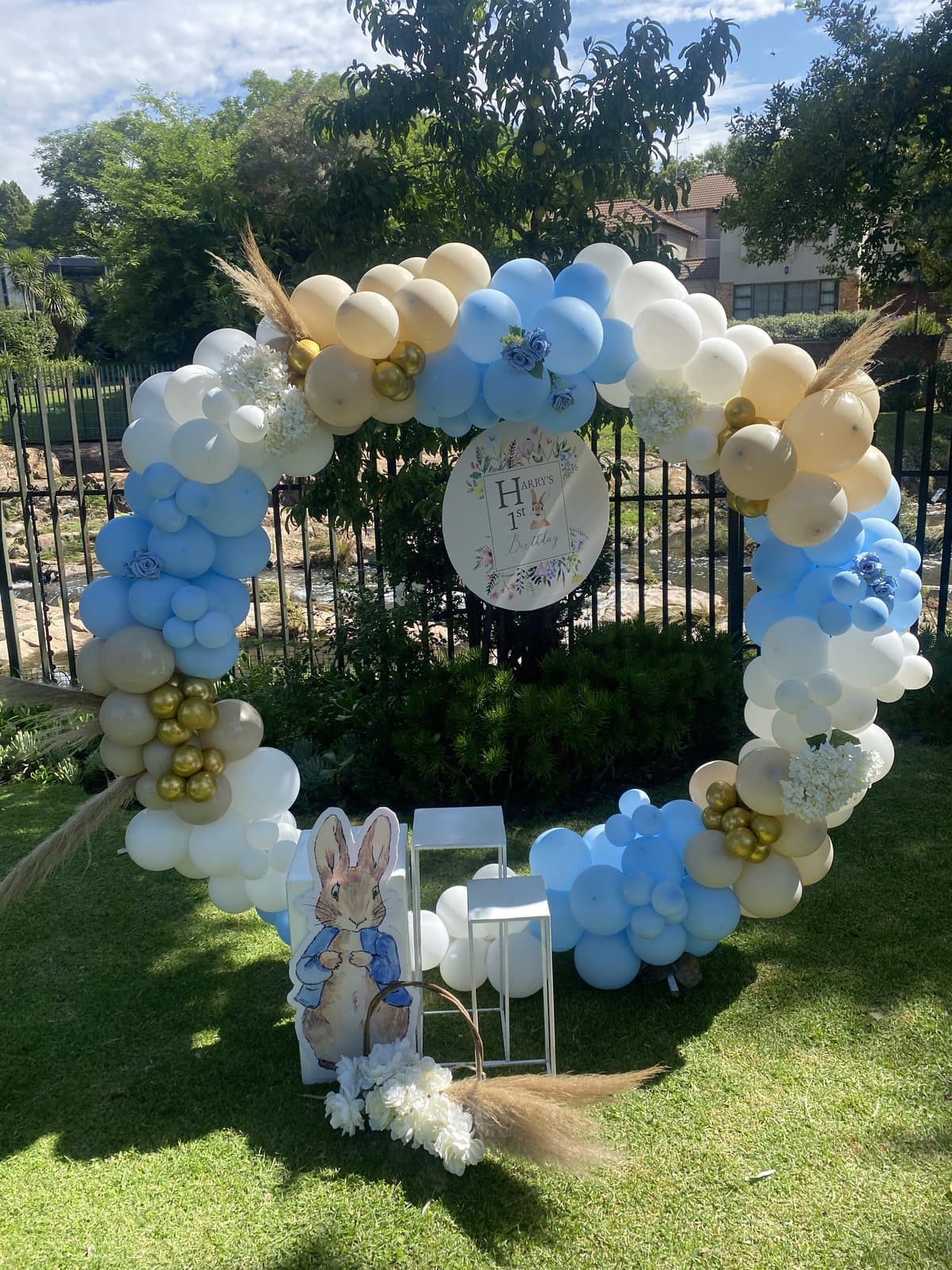 Pastel blue and cream balloon wreath arch with a bunny cutout in a garden