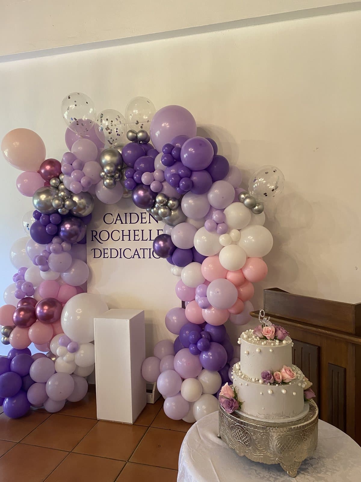 Purple and white balloon arch with a cake for a baby dedication celebration