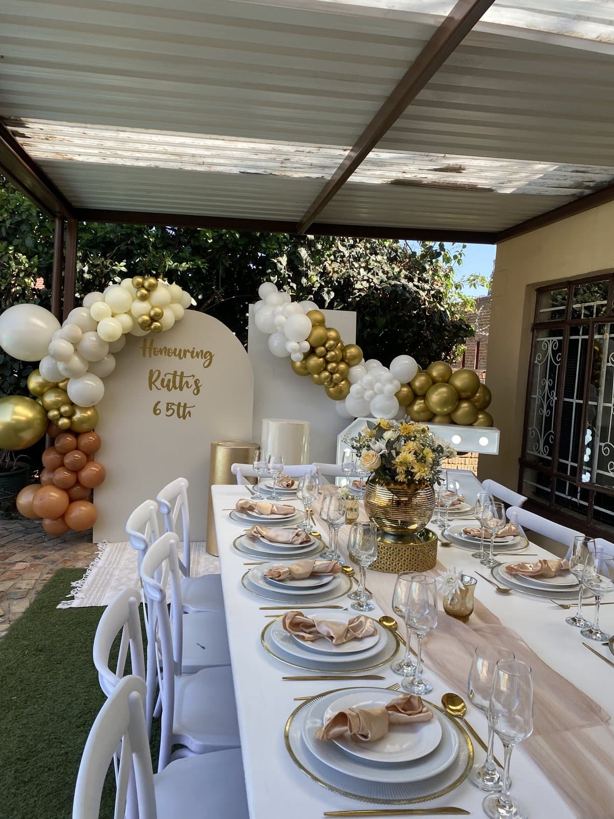 Elegant white and gold table setting with a balloon arch for a milestone birthday