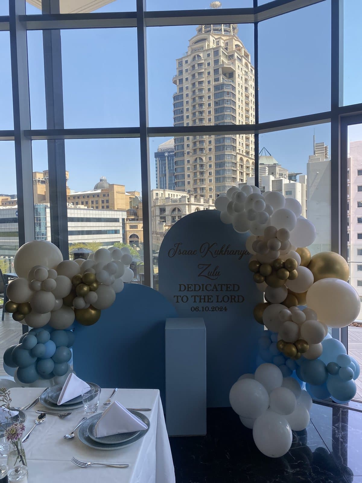Blue and white cloud balloon arch indoors with a city view
