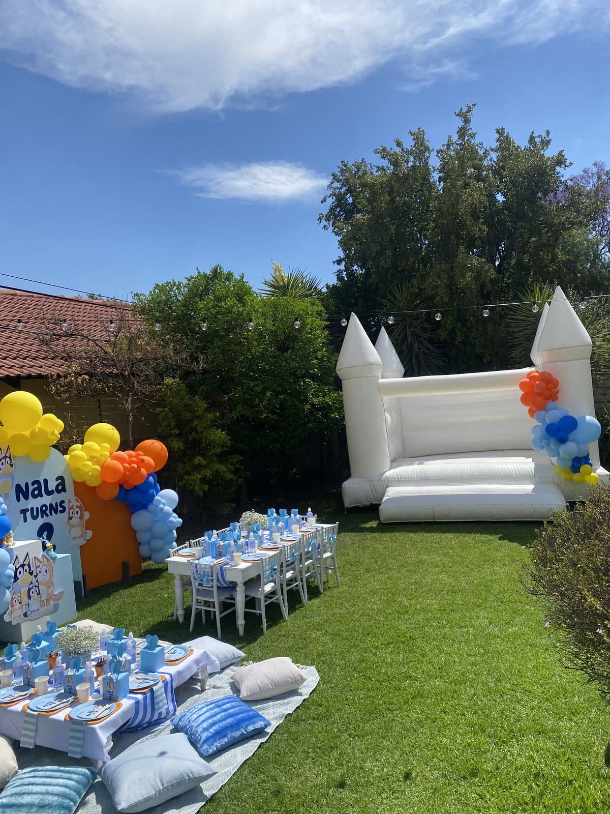 White bounce castle with a pastel balloon garland and gift table set up in a garden