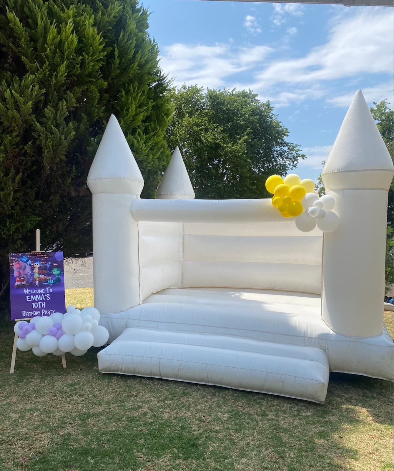 White bounce castle with purple and yellow balloon garland for a 10th birthday party