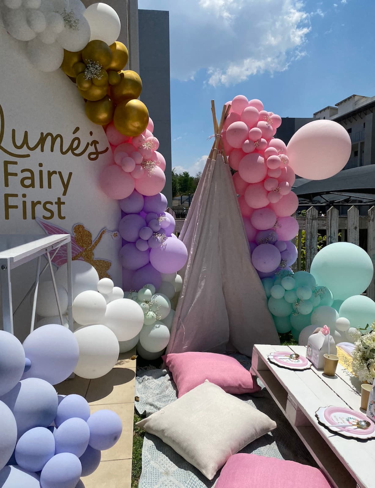 Pink, purple and gold balloon garland with a teepee picnic setup for a fairy themed first birthday