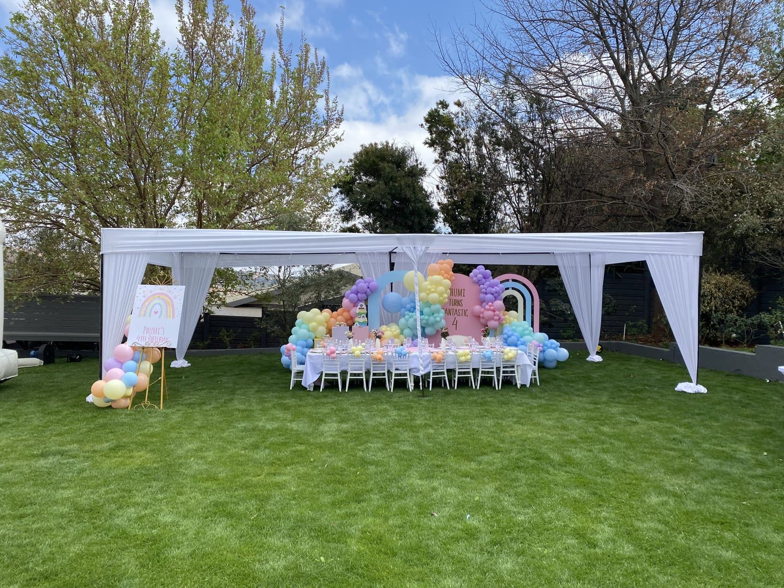 White marquee arch with a pastel balloon table setup in a garden