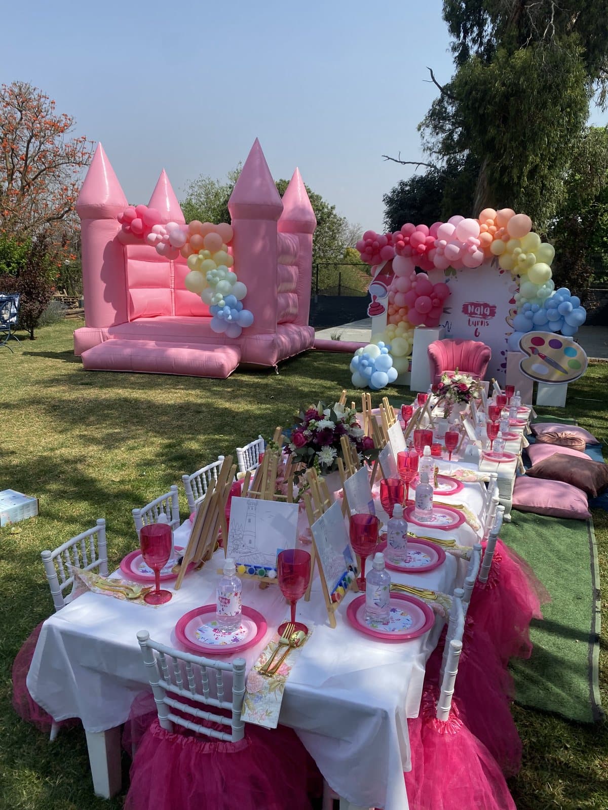 Pink princess castle bounce house with a balloon arch and pastel table setting