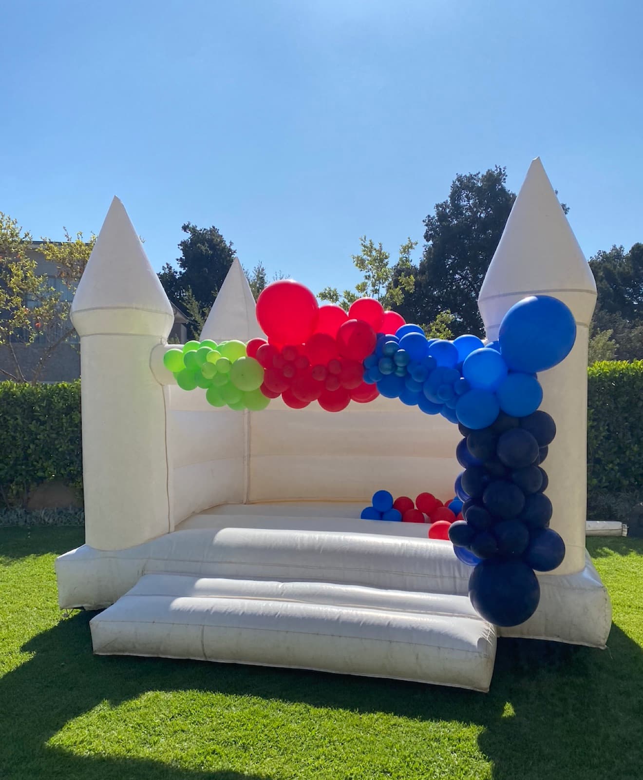 White bounce castle decorated with a rainbow balloon garland