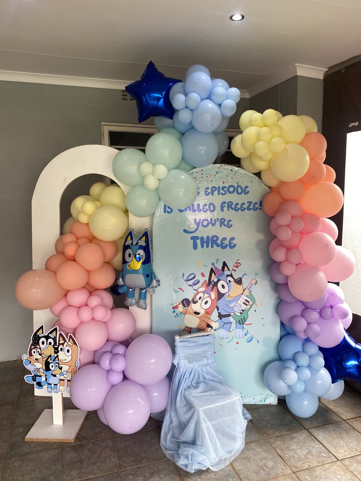 Pastel rainbow balloon arch with character cutouts for a birthday party