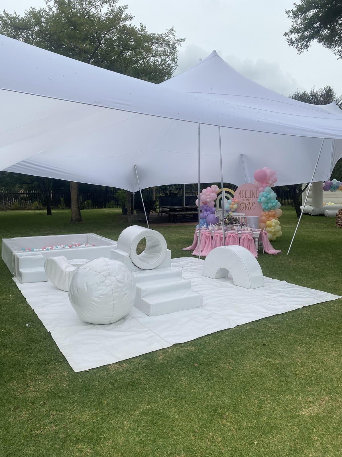 White tent with a pastel balloon corner set up for a picnic-style party