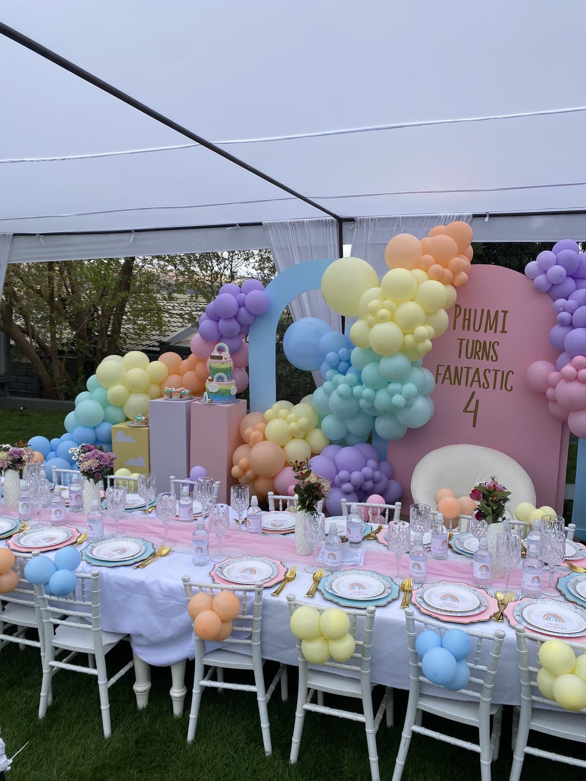 Pastel rainbow balloon arch with an outdoor tablescape for a fourth birthday