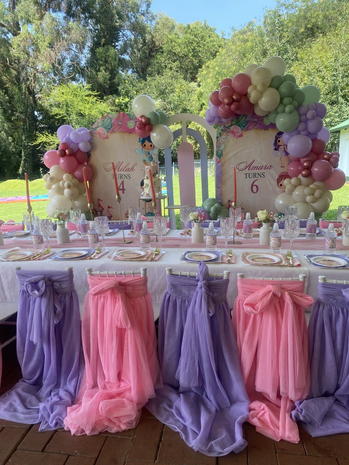 Colourful floral balloon arch with purple chair drapes under a thatch roof