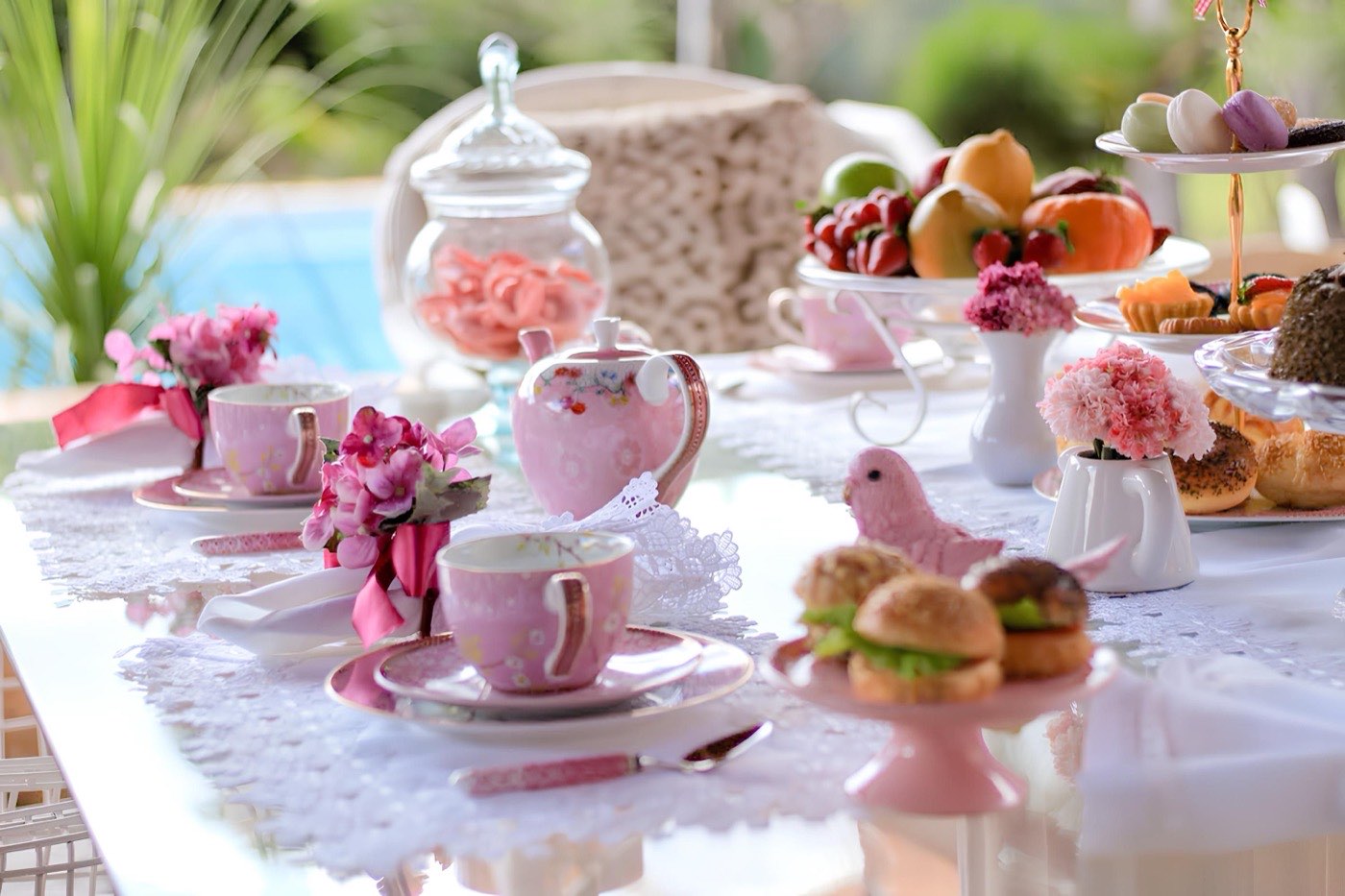 A pink high tea table set with floral teacups, macarons, fruit and finger sandwiches