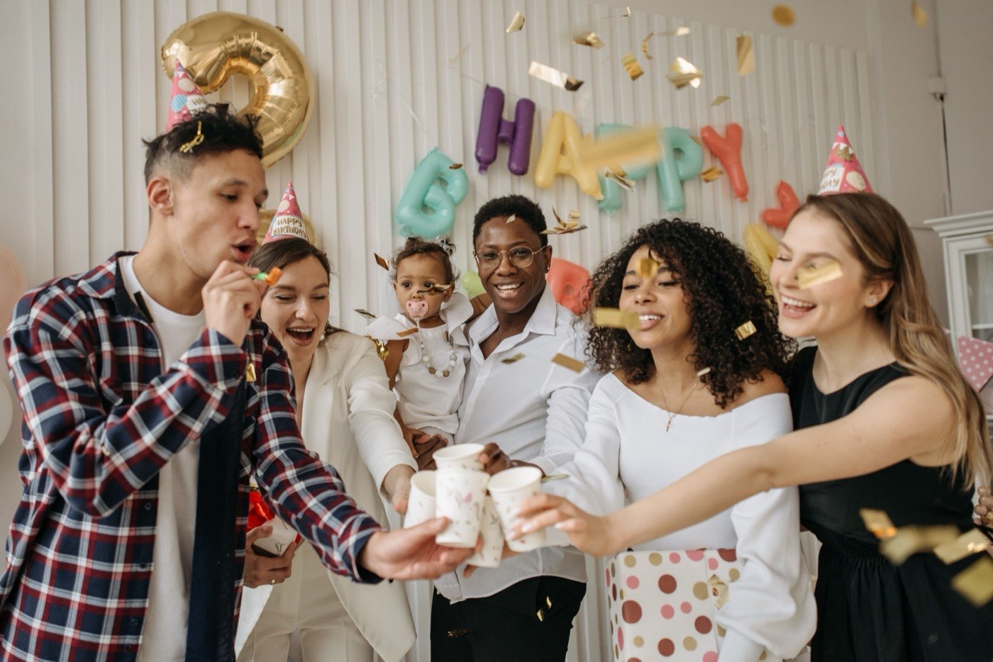 A multi-generational family celebrating together under a Happy Birthday balloon banner
