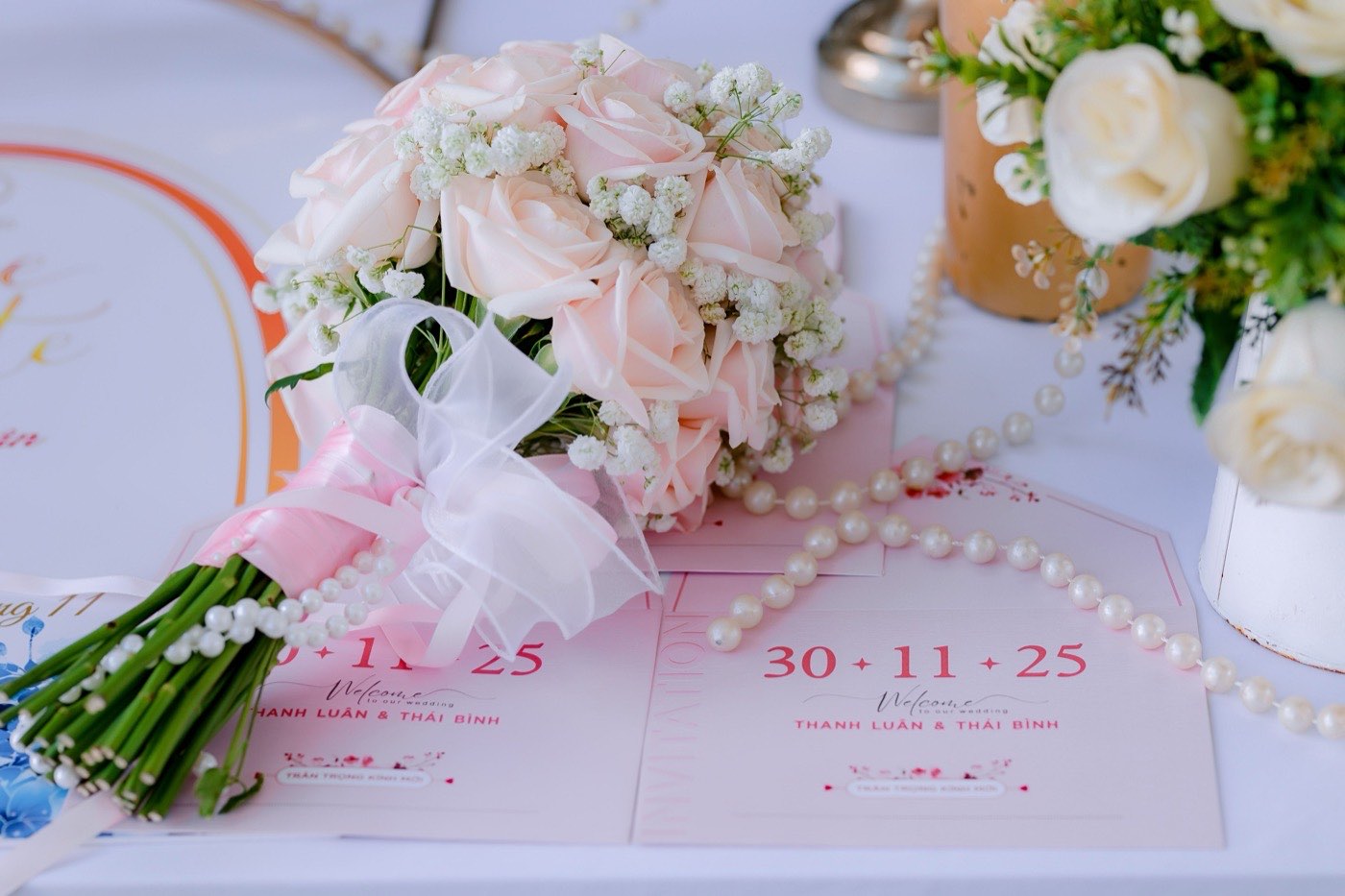 Printed wedding invitation cards laid out with pink roses and a pearl necklace
