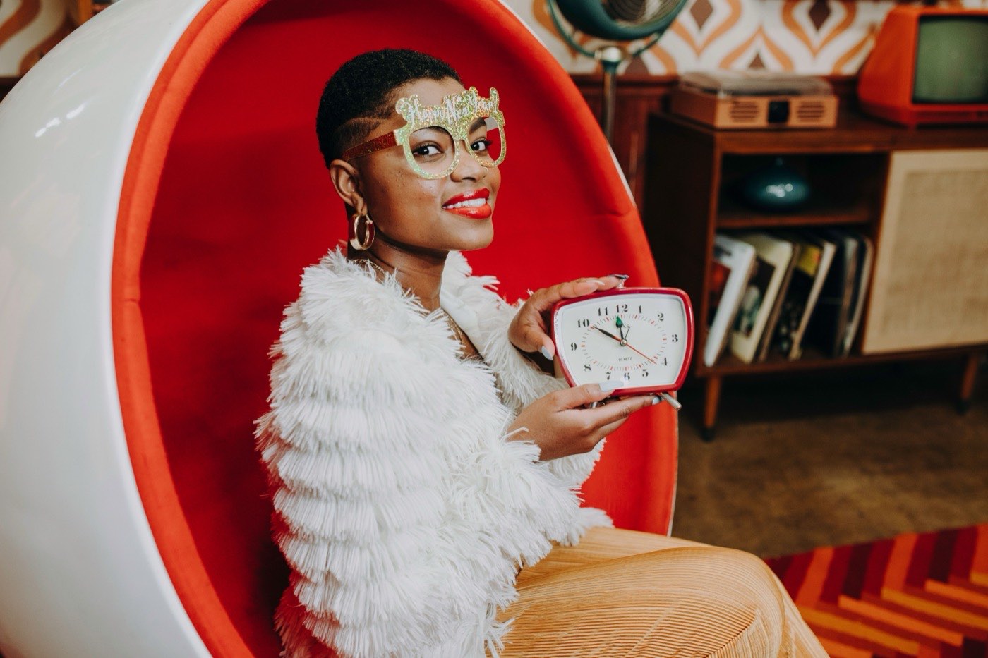 A woman holding a vintage red alarm clock, playfully checking the time