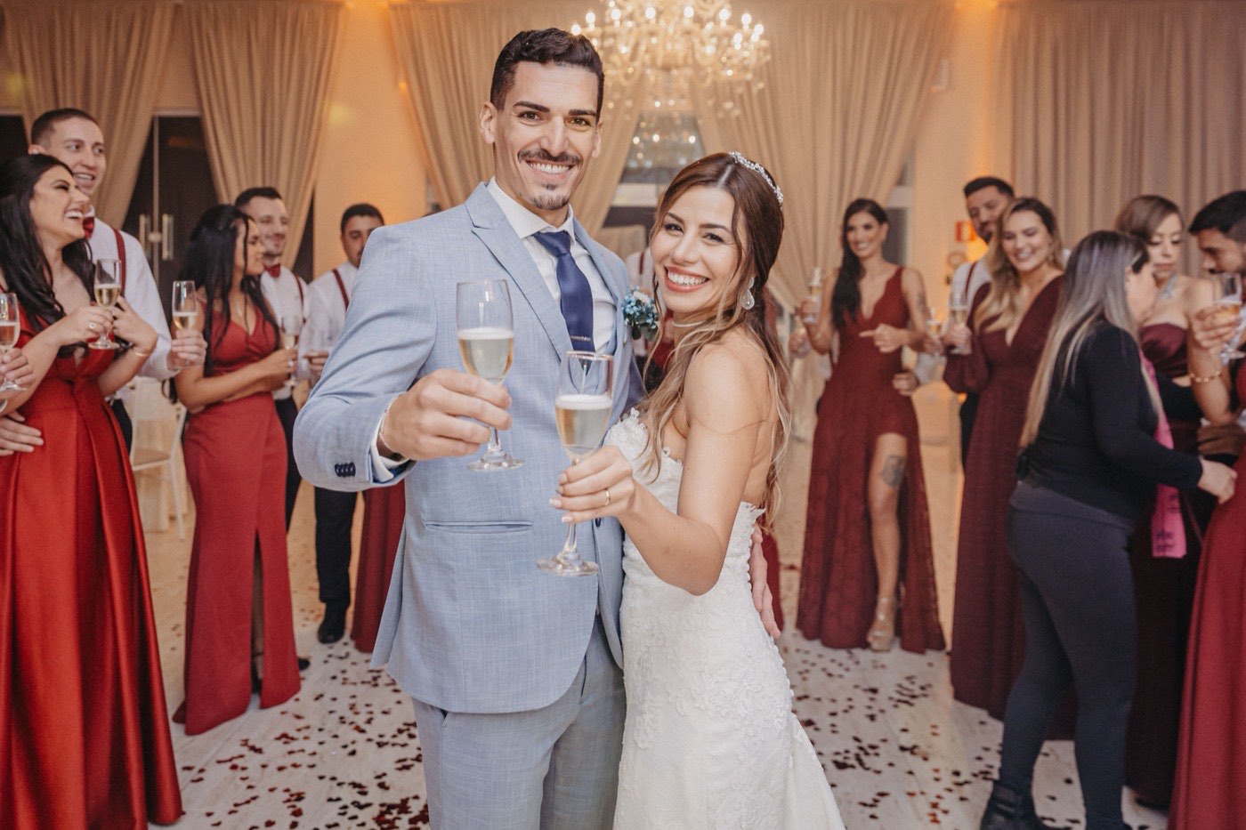 A bride and groom toast with champagne surrounded by their smiling wedding party