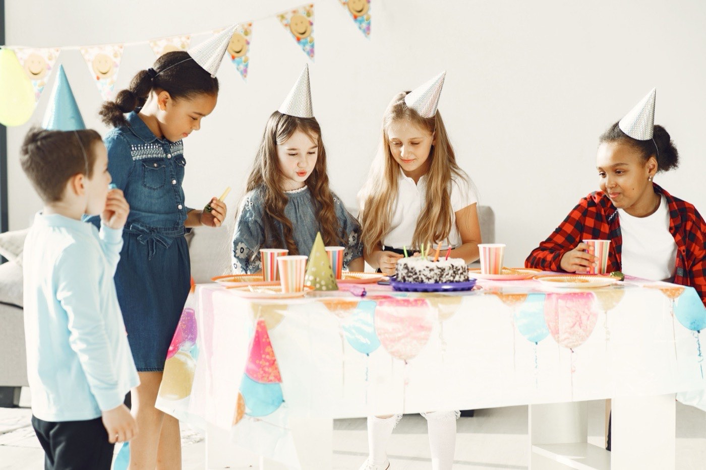 Children in party hats gathered around a birthday cake at a decorated table