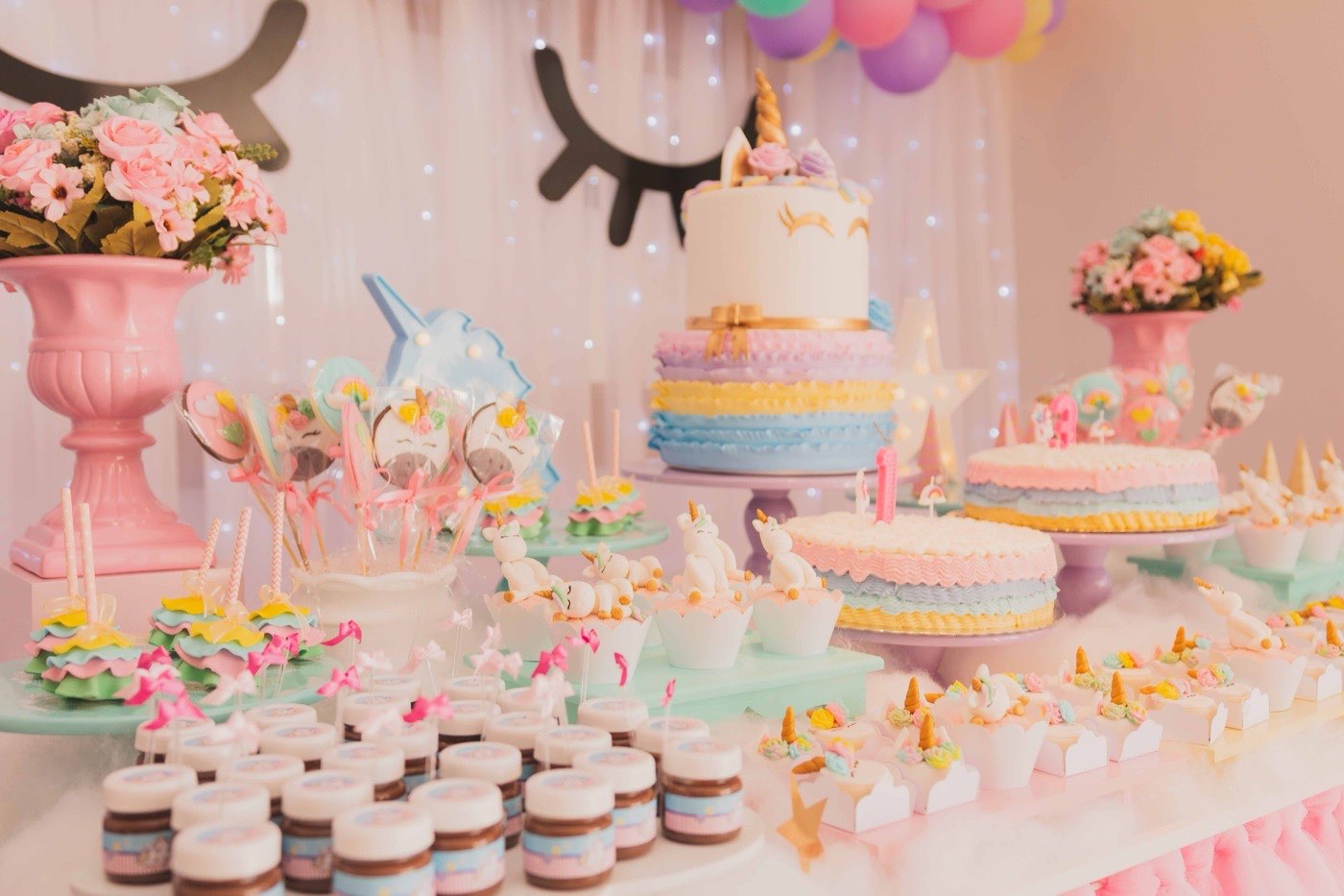 A pastel unicorn themed birthday dessert table with a tiered cake and matching treats