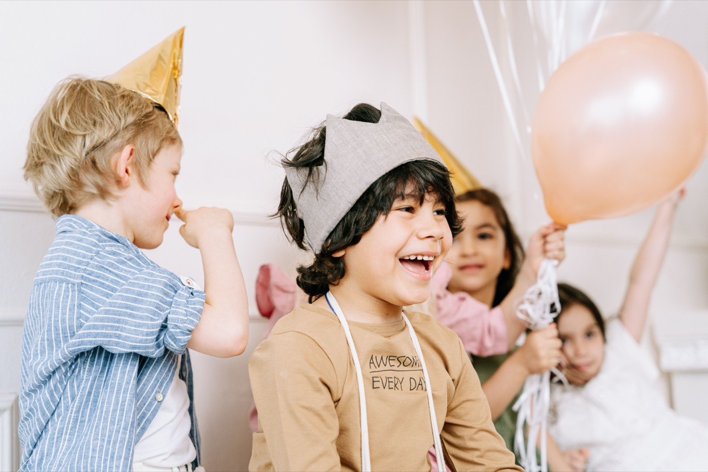 Children in paper party hats laughing together with balloons at a birthday party