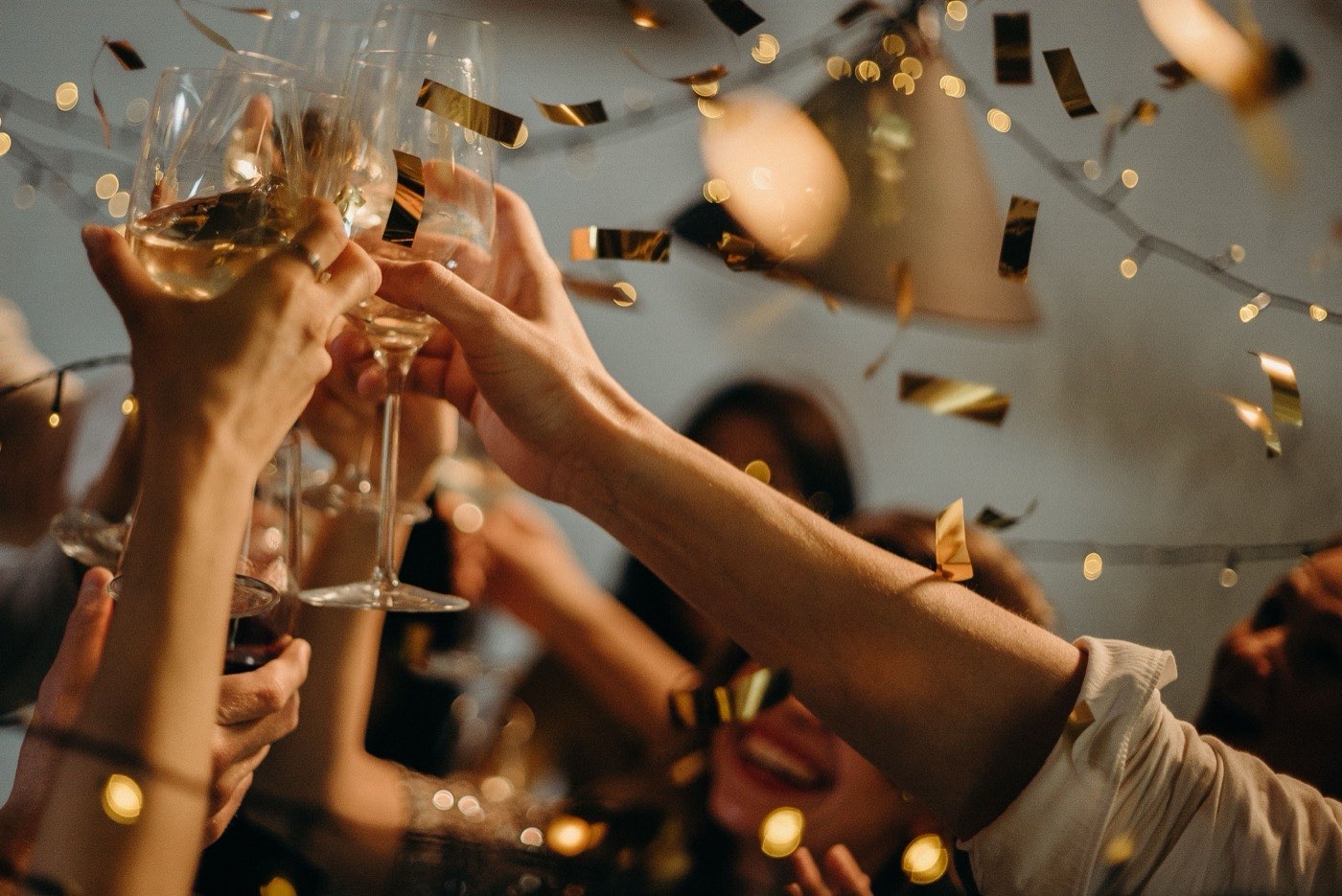 Friends clinking wine glasses together at a party with gold confetti falling